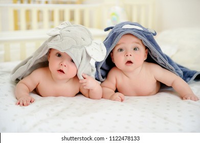 Adorable five months old baby boy twins in character towels after taking a bath or shower, in bed at home. Nursery for children. Tummy time activities for infants