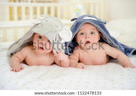Adorable five months old baby boy twins in character towels after taking a bath or shower, in bed at home. Nursery for children. Tummy time activities for infants