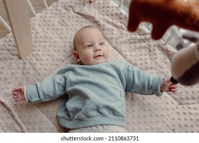 Adorable four month old baby boy laying in play pen looking around smiling. Wears a blue sweater and has blue eyes. - Shutterstock ID 2110863731
