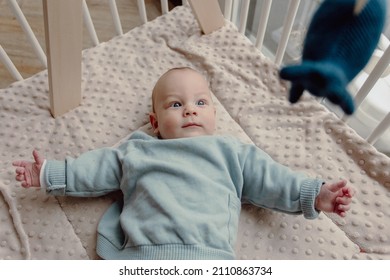 Adorable four month old baby boy laying in play pen looking around smiling. Wears a blue sweater and has blue eyes. - Shutterstock ID 2110863734