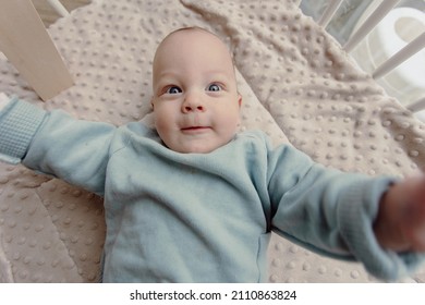 Adorable four month old baby boy laying in play pen looking around smiling. Wears a blue sweater and has blue eyes. - Shutterstock ID 2110863824