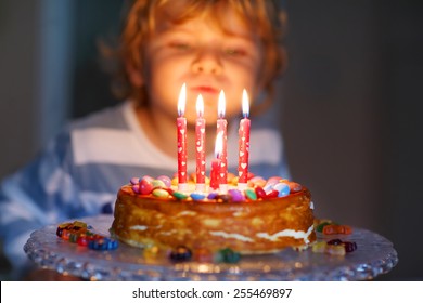 Adorable Four Year Old Kid Celebrating His Birthday And Blowing Candles On Homemade Baked Cake, Indoor. Birthday Party For Kids. Focus On Child