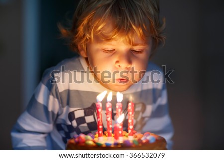 Adorable four year old kid celebrating his birthday and blowing candles on homemade baked cake, indoor. Birthday party for kids.