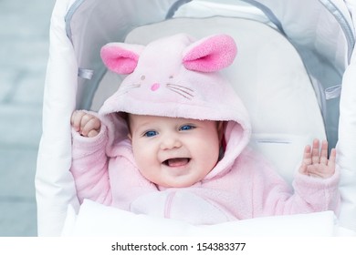 Adorable funny baby girl wearing a pink warm bunny snow suit sitting in a white stroller on a walk in a winter park