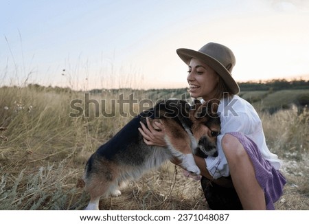 Adorable funny Welsh Corgi dog joyfully jumping onto its owner woman amidst a vibrant field.