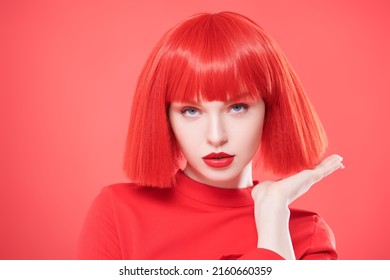 Adorable girl with bright red lips and red hair. Red studio background. Beauty, makeup. Hairstyle, hair coloring. Fashionable red colour.