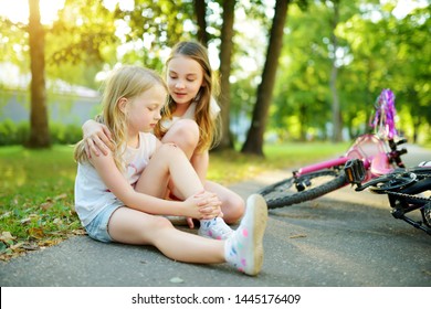 Adorable Girl Comforting Her Little Sister After She Fell Off Her Bike At Summer Park. Child Getting Hurt While Riding A Bicycle. Active Family Leisure With Kids.