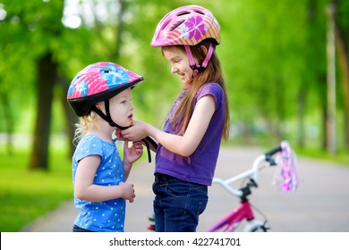 Adorable girl helping her little sister to put a bicycle helmet on