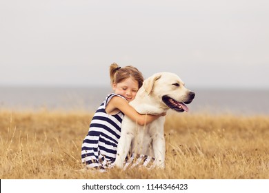 adorable girl hugging her labrador retriever. happy kid with big white dog outdoors. child and her dog best friend having fun in the garden. girl with cute family dog. 