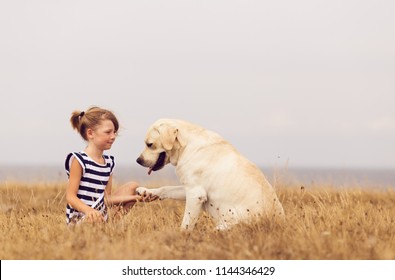 adorable girl hugging her labrador retriever. happy kid with big white dog outdoors. child and her dog best friend having fun in the garden. girl with cute family dog. 