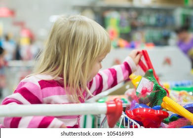 Adorable Girl Look To Toys Sit In Shopping Cart In Supermarket