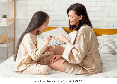 Adorable girl painting her mother's nails with polish on bed at home. Young lady and her daughter having fun, making manicure at domestic beauty spa salon. Friendship between parent and child - Powered by Shutterstock