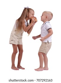 An Adorable Girl With Ponytails And A And A Laughing Boy Sharing A Cinnamon Bun Isolated On A White Background. Beautiful Little Siblings In Matching Clothes Eating Having Fun And Eating Sweets.