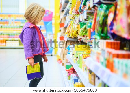 Adorable girl select sweet on shelves in supermarket
