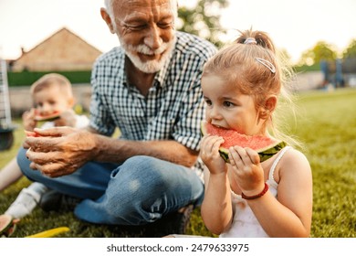 Adorable girl sitting in backyard with sibling and granddad and eating fresh ripe watermelon and enjoying summertime. - Powered by Shutterstock