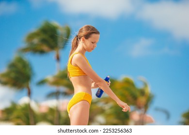 Adorable girl sprays protective cream on her body on a hot day. Sun protection