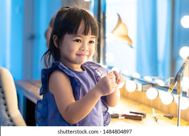 Adorable happy Asian little girl trying makeup in front of the mirror in dressing room