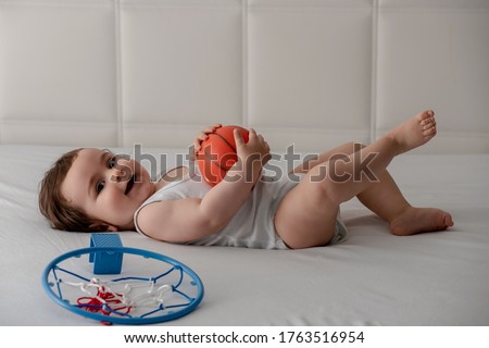 Adorable and happy baby boy playing with basketball on the bed.