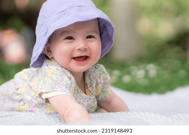 adorable and happy baby girl in summer hat embraces the joys of playfulness on a soft blanket. Laughing as she explores the natural wonders of an outdoors city park - Shutterstock ID 2319148493