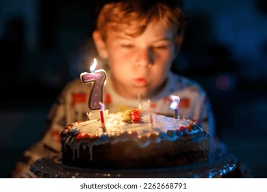 Adorable happy blond little kid boy celebrating his birthday. Child blowing seven candles on homemade baked cake, indoor. Birthday party for school children, family celebration of 7 years - Powered by Shutterstock