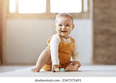 Adorable happy blonde infant baby playing with kids toys at home while sitting on carpet floor in living room. Portrait of smiling cute child toddler using colorful toys, copy space