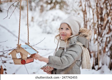 Adorable Happy Child Girl With Bird Feeder In Winter Garden