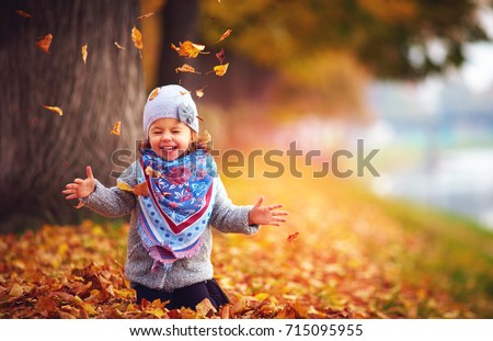 adorable happy girl playing with fallen leaves in autumn park