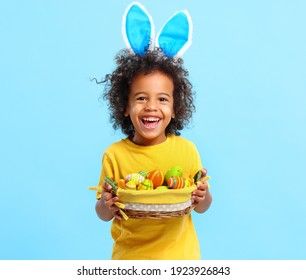 Adorable happy little African American boy with curly hair in casual clothes and bunny ears on head laughing while holding Easter basket - Powered by Shutterstock