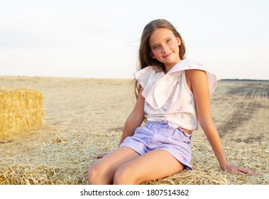 Adorable Happy Smiling Ittle Girl Child Sitting On A Hay Rolls In A Wheat Field At Sunset
