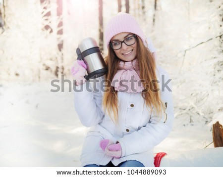
Adorable happy young blonde in pink knitted hat scarf holding a hot mug sitting in a snowy winter forest