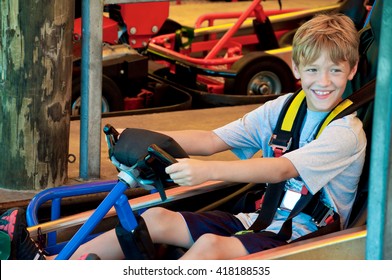 Adorable Happy Young Kid On A Go Cart At An Amusement Park Looking Sideways.