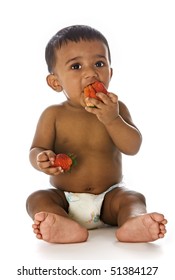 Adorable Healthy Indian Baby Sitting On Floor And Eating Strawberries, Isolated On White Background.