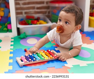 Adorable hispanic baby playing xylophone lying on floor at kindergarten - Shutterstock ID 2236993131