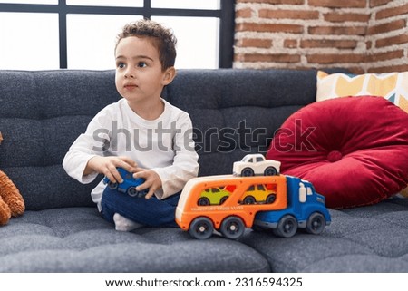 Adorable hispanic boy playing with car toy sitting on sofa at home