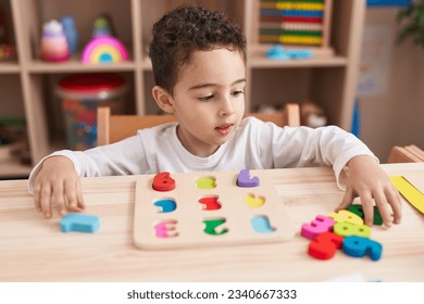 Adorable hispanic boy playing with maths puzzle game sitting on table at kindergarten - Powered by Shutterstock