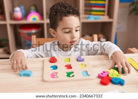 Adorable hispanic boy playing with maths puzzle game sitting on table at kindergarten