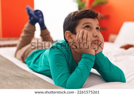 Adorable hispanic boy smiling confident lying on bed at bedroom