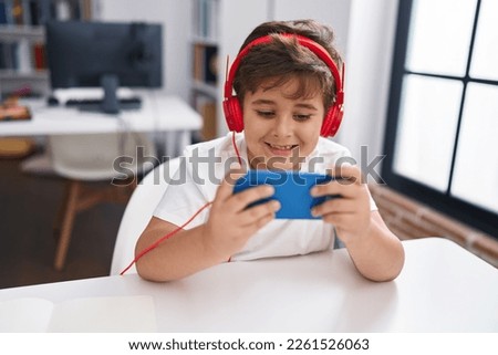 Adorable hispanic boy student using smartphone and headphones at classroom