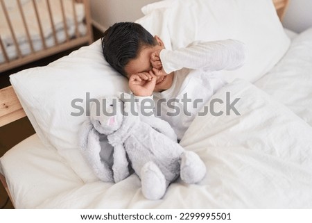 Adorable hispanic boy waking up rubbing eyes at bedroom
