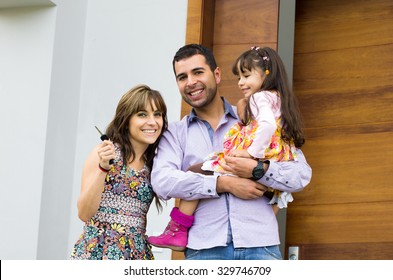 Adorable Hispanic Family Of Three Posing For Camera Outside Front Entrance Door.