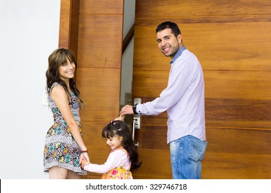 Adorable Hispanic Family Of Three Posing For Camera Outside Front Entrance Door While Entering House.