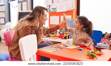 Adorable hispanic girl playing with maths puzzle game high five with teacher at kindergarten
