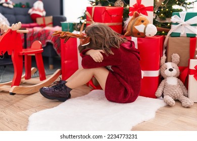 Adorable hispanic girl sitting on floor by christmas tree crying at home