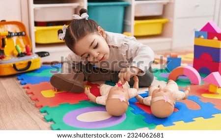 Adorable hispanic girl sitting on floor playing with baby doll at kindergarten