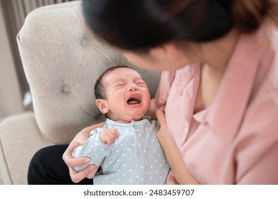 An adorable infant baby son is crying in his mother arms, feeling uncomfortable or hungry. childhood, milk feeding, breastfeeding - Powered by Shutterstock