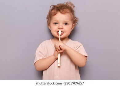 Adorable infant little girl holding toothbrush isolated on gray background brushing her teeth with tiny toothbrush looking at camera children oral care. - Powered by Shutterstock