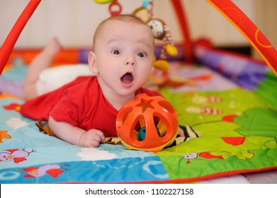 Adorable infant lying on colorful baby play mat with toys. Child early development and activity space. Tummy time fun