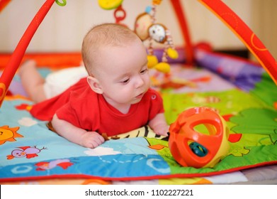 Adorable infant lying on colorful baby play mat with toys. Child early development and activity space. Tummy time fun