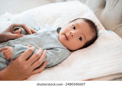 An adorable, innocent Asian newborn baby son in blue pajamas is in his bed, talking and playing with his mom. infant, toddler, child - Powered by Shutterstock