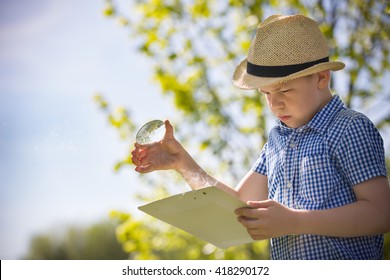 Adorable kid boy making fire on paper with a magnifying glass outdoors, on sunny day. Child exploring fire nature in the garden. Young explorer with magnifier. Education and discovery concept